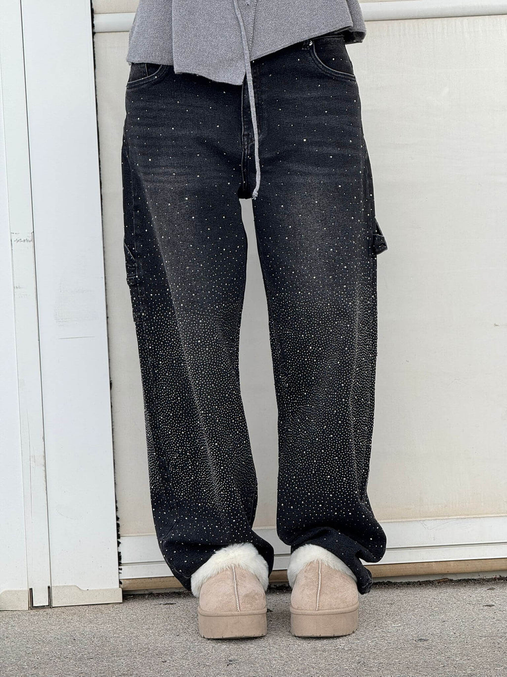 Jeans neri con dettagli glitterati, indossati con scarpe beige invernali. Moda casual, pantaloni decorati, stile urbano.
