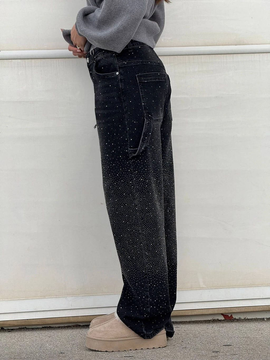 Pantaloni neri a vita alta con dettagli glitterati, tasche posteriori, indossati da una persona. Scarpe beige con suola spessa. Moda casual elegante.