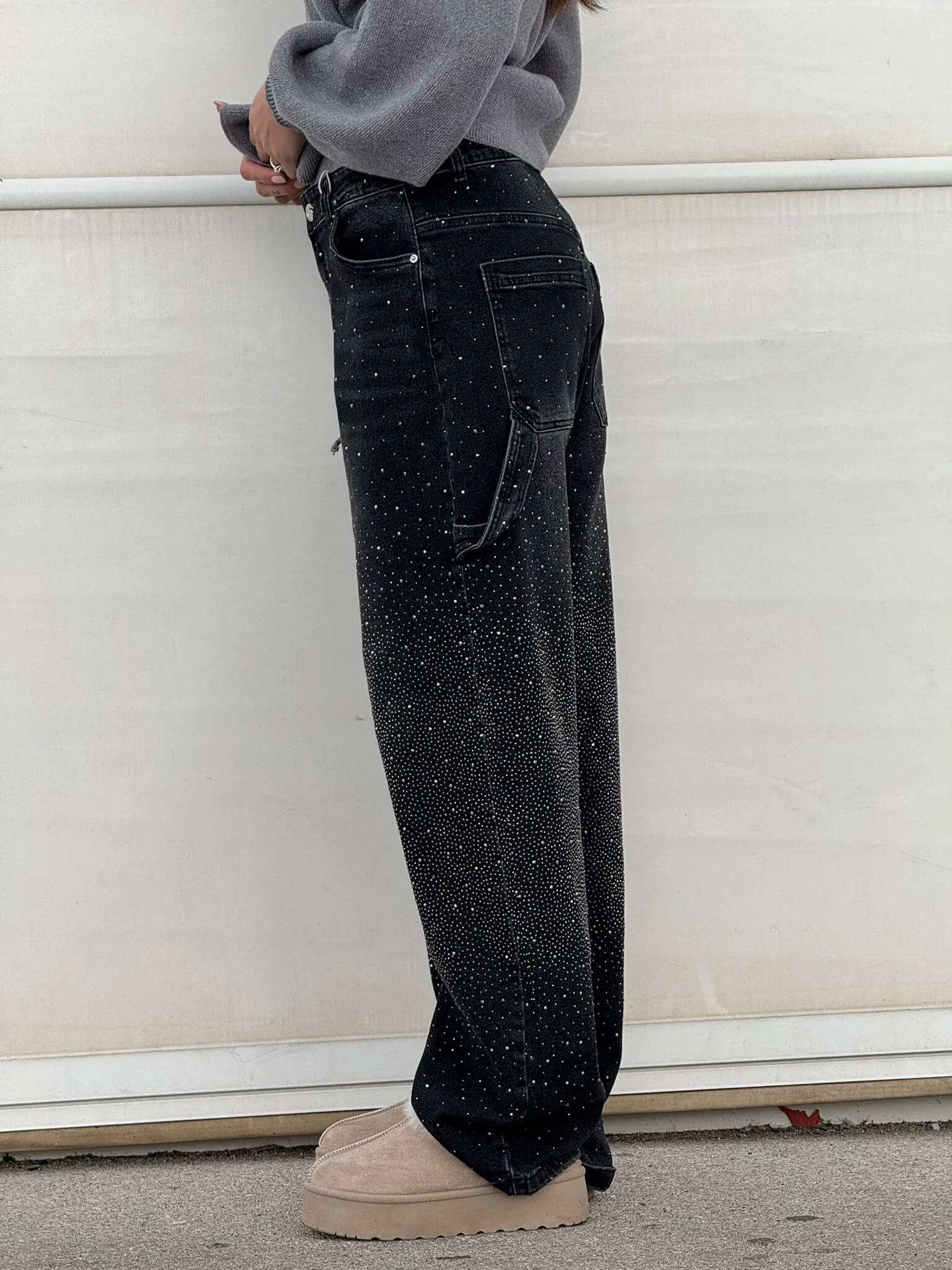 Pantaloni neri a vita alta con dettagli glitterati, tasche posteriori, indossati da una persona. Scarpe beige con suola spessa. Moda casual elegante.