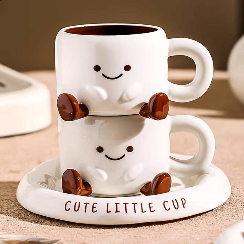 Two white mugs with smiling faces, stacked on a matching coaster, on a wooden surface.